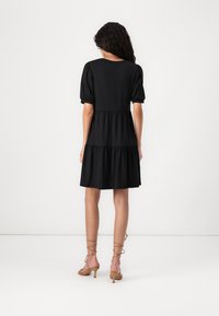 Vestido preto curto com mangas bufantes, design em camadas e tecido suave. A parte de trás apresenta um decote arredondado e termina acima do joelho.