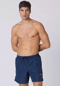 Pantaloni da bagno blu navy con vita elasticizzata e cordino. Presentano un logo ricamato sul lato sinistro. Il materiale sembra leggero e liscio.