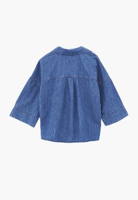 Blå denimjakke med en boxplisse-detalje på ryggen og brede trekvartlange ærmer.