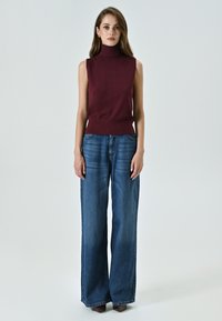 Bordeauxfarbenes ärmelloses Rollkragenoberteil, kombiniert mit weiten blauen Jeans. Das Top hat eine taillierte Passform, und die Jeans sind lässig geschnitten.