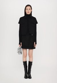 Black cropped jacket with short sleeves, paired with a textured black skirt, knee-high black boots, and a silver handbag. Simple design.