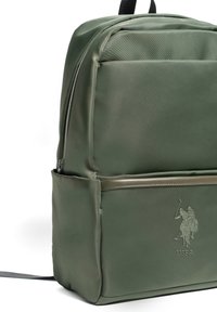Zielony plecak wykonany z gładkiego nylonu o matowym wykończeniu. Posiada przednią kieszeń, górny zamek błyskawiczny oraz wytłoczone logo na przodzie.