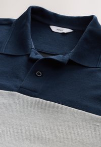 Marineblaue und graue gestreifte Poloshirt aus strukturiertem Stoff; verfügt über einen klassischen Kragen und zwei Knöpfe am Hals. Markenetikett sichtbar.