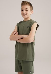 Olivgrön ärmlös t-shirt och matchande shorts, tillverkade av mjukt tyg, med en liten svart logotyp på vänster bröst och shorts.