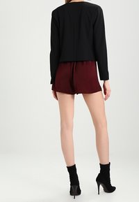 Veste noire courte portée sur un short bordeaux, associée à des bottines noires montantes. Accent sur les lignes épurées et le contraste de textures entre les matériaux.