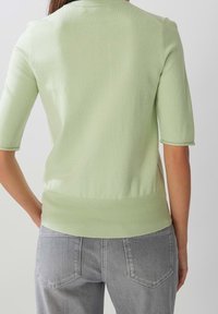 Pull vert clair à manches courtes en tricot lisse, avec un ourlet et des poignets côtelés, associé à un jean en denim gris.