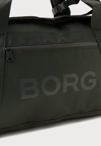 Σκούρο πράσινο σακίδιο αθλητικών ειδών με μαύρους φερμουάρ, διχτυωτές ιμάντες ώμου και το λογότυπο "BORG" τυπωμένο στην μπροστινή τσέπη.