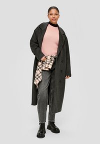 Manteau long gris, pull à côtes rose, jean noir et bottes noires à semelles épaisses. Chemise à carreaux nouée à la taille. Texture lisse, coupe décontractée.