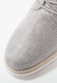 Baskets gris clair avec une tige en mesh texturé et scintillant, une semelle style espadrille beige, et des détails de couture subtils.