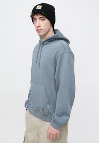 Szara bluza z kapturem, kieszenią kangurką i prążkowanymi ściągaczami. Czarna czapka typu beanie z naszywką z logo. Wykonana z miękkiej, teksturowanej tkaniny.