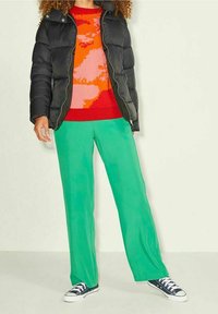 Black puffer jacket, vibrant red and pink patterned sweater, and green wide-leg pants, complemented by navy sneakers. Soft textures and bold colors.