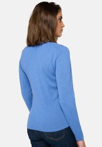 Pull en tricot bleu à manches longues, design ajusté, col rond et texture lisse, associé à un jean foncé. Vue arrière présentée.