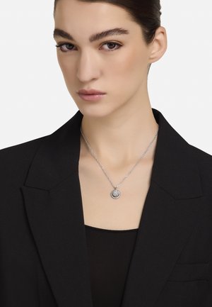 Colier argintiu cu pandantiv rotund cu model texturat, atârnat de un lanț delicat, purtat peste un top negru.