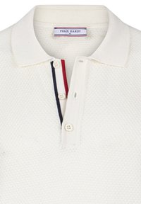 Camisa polo color crema con un tejido texturizado, tapeta de tres botones y rayas en rojo y azul marino contrastantes debajo del cuello. Etiqueta de la marca visible.