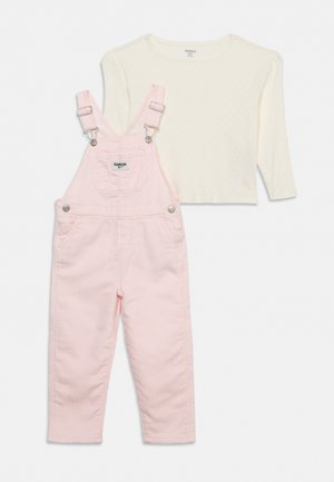 Salopette rose à rayures pour enfant, avec une poche avant et des bretelles réglables, associée à une chemise à manches longues couleur ivoire.