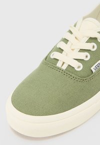 Gröna canvas sneakers med krämfärgade snören och gummisula. Har strukturerad tyg och en sidologotyp. Rundad tå och platt design.