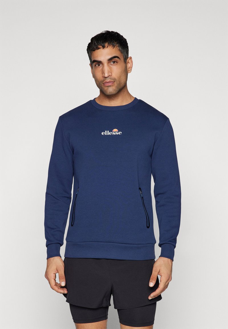 Granatowy sweter wykonany z miękkiego materiału, z okrągłym dekoltem, z logo na piersiach oraz zapinanymi na zamek kieszeniami po bokach.