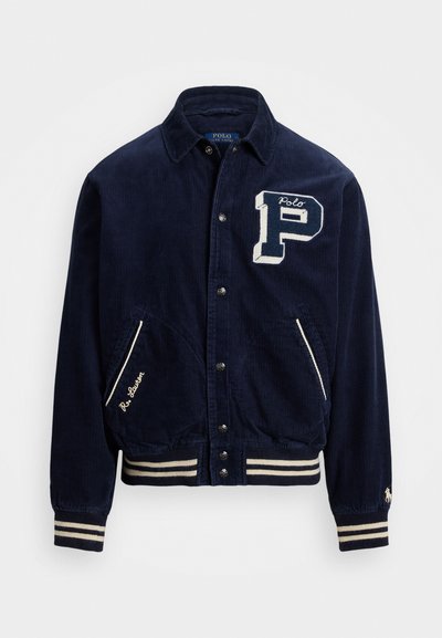 Navy corduroy jacket with white embroidered "P" and "Polo" details, buttoned front, two side pockets, and striped ribbed cuffs and hem.