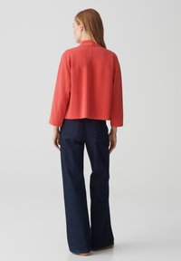 Veste courte corail avec un col haut et des manches longues, accompagnée d'un pantalon large bleu marine. Tissu lisse avec des détails matériels minimaux.
