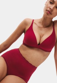 Rød bh og højtaljede trusser, begge i blødt bomuldsstof. Bh'en har justerbare stropper og et trekantet kopdesign; trusserne har en blondekant.