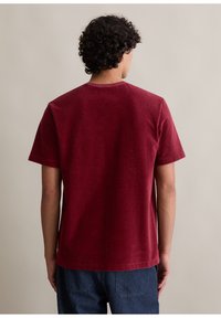 Burgundowa koszulka z krótkim rękawem, wykonana z miękkiej bawełny, z okrągłym dekoltem i luźnym krojem. Gładka tekstura z minimalną ilością szwów.