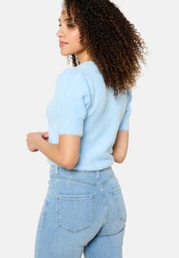 Light blue fluffy short-sleeve sweater with ribbed cuffs, paired with high-waisted light blue denim jeans featuring back pockets.