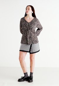 Bluzka w panterkę z wiązanym przodem, zestawiona z spódnicą w wzór houndstooth. Całość dopełniają czarne buty i szare skarpetki.