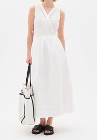 Abito bianco senza maniche a portafoglio con cintura in vita, dettagli di cuciture verticali, abbinato a una borsa a tote con accenti neri e sandali neri scivolati.