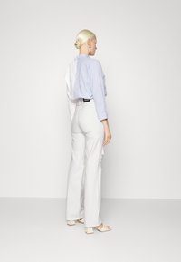 Camisa listrada azul claro com mangas longas, painel branco nas costas, combinada com calças largas brancas de cintura alta e sandálias de salto bloco.