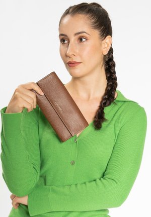 Brown textured leather wallet held in a hand, featuring a sleek design and a horizontal seam, against a background of a green sweater.