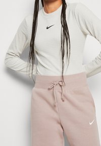 Ljust grå, ribbad långärmad tröja med en svart Nike-logotyp, parat med mjuka, rosiga joggingbyxor med elastisk midja och snörning.