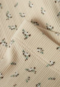 Bežani rebrasti materijal s malim cvjetnim uzorcima u zelenoj, smeđoj i bijeloj boji. Glatka tekstura s vidljivim detaljima šivanja.