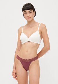 Soutien-gorge blanc rembourré avec bretelles ajustables et décolleté en V profond, associé à un string en dentelle bordeaux avec des accents en dentelle florale.