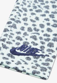 Skarpety Nike w jasnoniebieskiej bazie z teksturowanym wzorem i ciemnoszarym wzorem w panterkę. Wyszywane logo w granatowym kolorze blisko dołu.