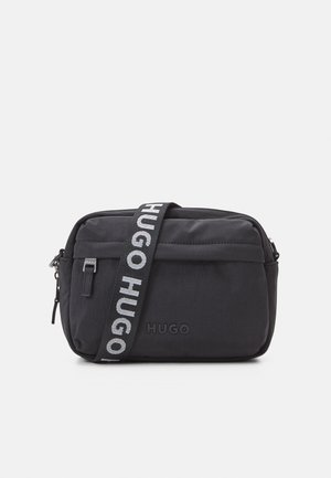 Czarna kompaktowa torebka na ramię z przednią kieszenią na zamek, paskiem z logo "HUGO" i wytłoczonym logo na przednim panelu.
