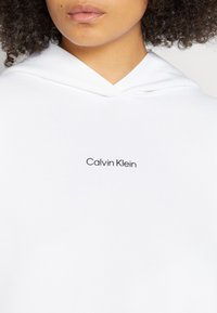 Sudadera blanca con un diseño minimalista y un logo negro de "Calvin Klein" en el frente. Fabricada en suave material de algodón.