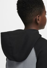 Sudadera con capucha que presenta una capucha y mangas negras, con un cuerpo gris. El material parece suave y se aprecian detalles de costura visibles en las costuras.
