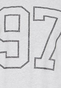 Pelēka kokvilnas T-krekls ar lielu melnu rhinestone ciparu "97" dizainu, ar gludu tekstūru un nedaudz stieptu audumu.