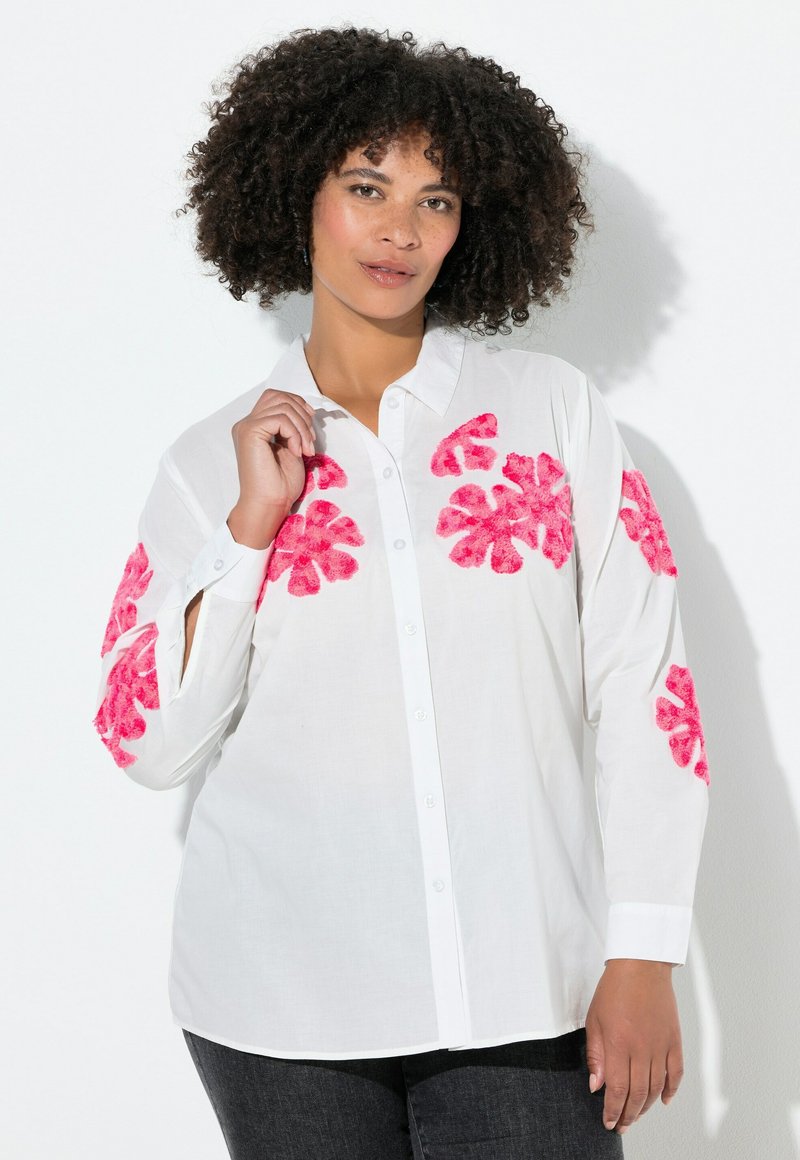 Chemise blanche à boutons avec des motifs floraux roses sur les manches. Elle possède un col, des manches longues et une coupe décontractée avec une texture lisse.