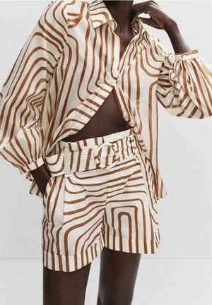 Mannequin portant une tenue crème avec des rayures abstraites marron, comprenant une chemise boutonnée à manches longues et un short taille haute ceinturé.