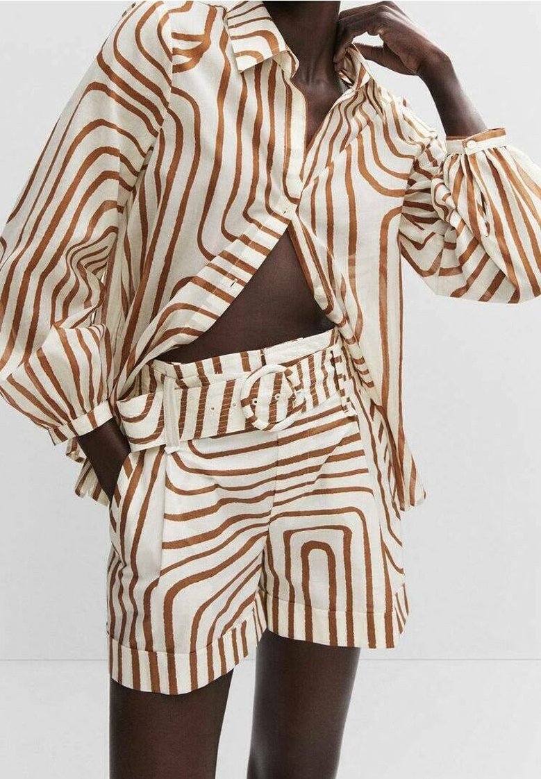 Mannequin portant une tenue crème avec des rayures abstraites marron, comprenant une chemise boutonnée à manches longues et un short taille haute ceinturé.