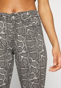 Jeans estampados de serpiente en gris y blanco, con un diseño ajustado, cinco bolsillos y un cierre de botón en la cintura.