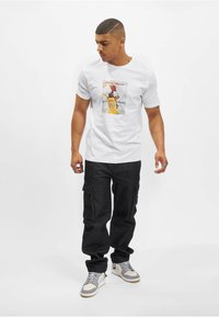 Hvid T-shirt med et farverigt grafisk print af en basketballspiller, parret med mørke cargo-bukser og grå sneakers. Enkel design.