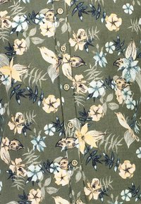 Tessuto a stampa floreale in verde con fiori gialli, blu e bianchi. Presenta piccoli bottoni lungo la parte anteriore. Texture morbida con un motivo naturale.