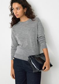 Grå strikket sweater med lange ærmer, parret med en skinnende sort clutch-taske. Sweateren har en simpel rund halsudskæring og en afslappet pasform.