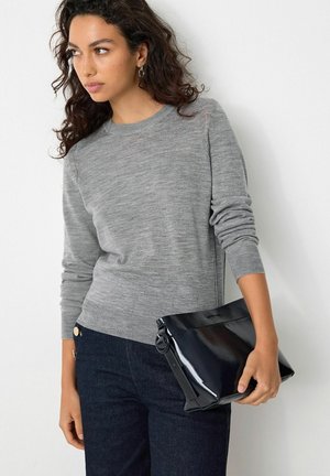 Pull en maille gris à manches longues, associé à un sac à main noir brillant. Le pull présente un col rond simple et une coupe décontractée.