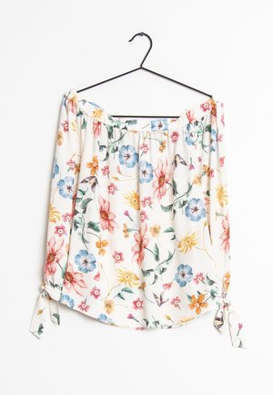 Biała bluzka z odkrytymi ramionami w wielokolorowy kwiatowy wzór, z długimi rękawami i wiązanymi mankietami, wisząca na czarnym wieszaku na białym tle.