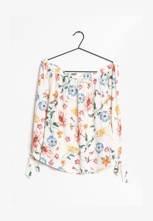 Biała bluzka z odkrytymi ramionami w wielokolorowy kwiatowy wzór, z długimi rękawami i wiązanymi mankietami, wisząca na czarnym wieszaku na białym tle.