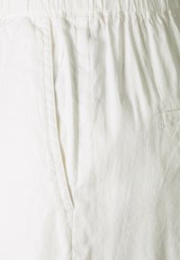 Biała tkanina o miękkiej strukturze, z marszczonym elastycznym pasem i kieszeniami bocznymi. Prosty i nieozdobiony design.