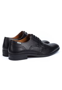 Scarpe in pelle nera con dettagli perforati, design con lacci e tacco basso. Presentano un logo discreto sul lato e una texture liscia.
